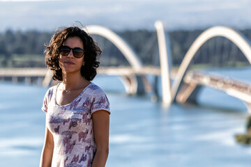 At the end of the afternoon a beautiful brunette woman walks near the bridge under the lake. Brazilian model. Golden hour. JK bridge. Brasília.