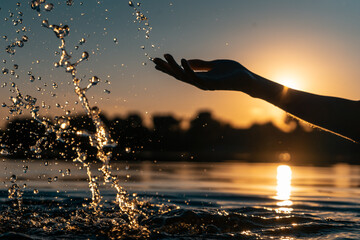 Obraz na płótnie Canvas closeup of girl hand silhouette play or splash water in lake on beach at sunset