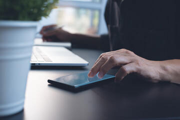 Fototapeta premium Man using mobile phone during working on laptop computer from home office