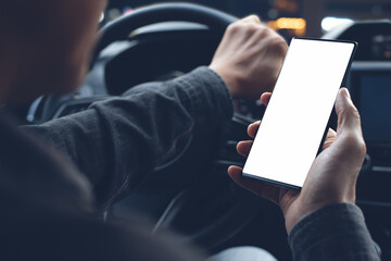 Mockup image of man hand holding and looking at blank screen mobile phone while driving a car at night