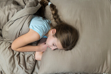 Girl with dark hair sleeps in brown bed