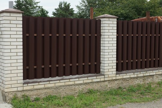 part of a wall of a fence made of brown metal and white bricks outside in green grass