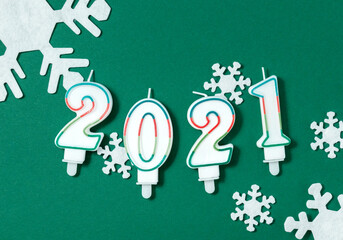 2021 New Year flat lay composition. Candles in shape of figures, white snowflakes decorations on green background. Christmas concept. Top view.