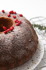 Festive bundt cake decorated with red berries and fir branches on white background.