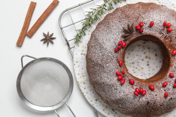 Festive bundt cake decorated with red berries and fir branches on white background.