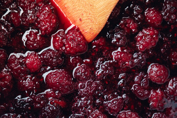 Close up of stirring blackberries and sugar making homemade blackberry jam with wooden utensil.