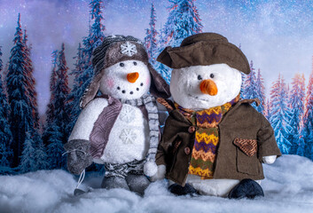Two stuffed snowmen on a winter background wearing warm winter clothes 