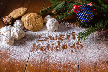 Obraz na płótnie Canvas Sweet holidays is written in sugar, and surrounded with home made cookies and fir branches and decorations for Christmas 