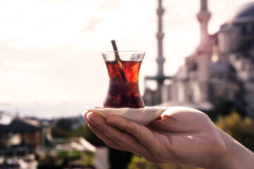 A glass of traditional Turkish tea in the hand of a young man. The Blue mosque in the sun rays on the background. Istanbul, Turkey