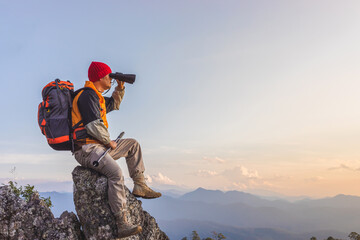 Hikers with backpacks holding binoculars sitting on top of the rock mountain