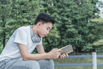 Fototapeta premium Young man sitting in the park is reading a book