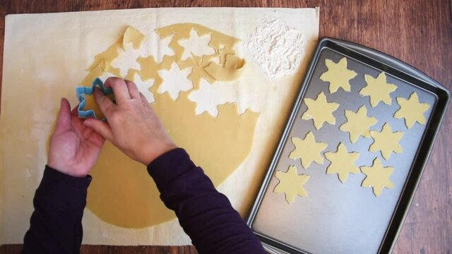 Woman’s hands cutting out star shaped sugar cookies and placing them on a baking sheet
