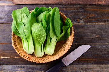 Fresh Bok Choy or Pak Choi (Chinese cabbage) in bamboo basket and kitchen knife on wooden background, Organic vegetables, Top view