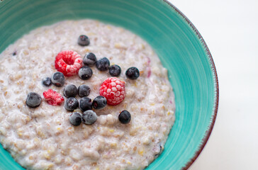 Oatmeal porridge in a plate with currant and raspberry berries.