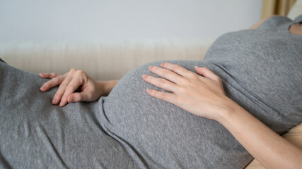 asian pregnant woman on sofa couch touching belly with care.