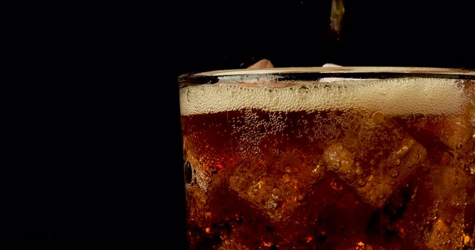 Truck shot of pouring carbonated drinks bubbles with ice cubes. Pouring soft drinks with ice and bubbles in glass on black background.