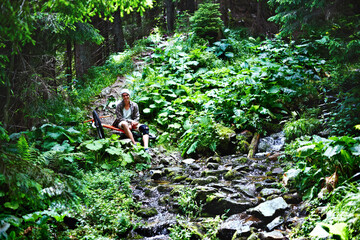 Young caucasian cyclist sitting near the bike in the summer mountain forest.