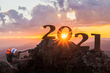 A silhouette of man with backpack climbing on rock and Happy New year 2021 letters on the mountain...