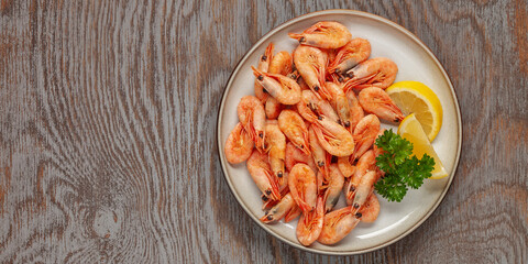 Boiled shrimp prawns in a shell with lemon and parsley in a plate on a wooden background. Top view