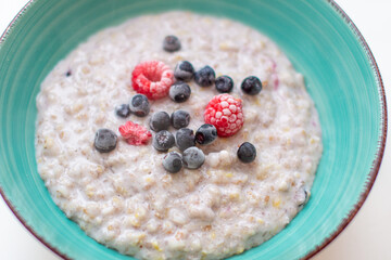 Oatmeal porridge in a plate with currant and raspberry berries.