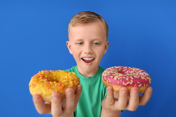 Funny little boy with donuts on color background