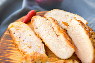 Board with cooked cut chicken fillet on dark background