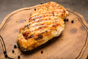 Board with cooked chicken fillet on dark background