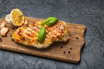 Board with cooked chicken fillet on dark background