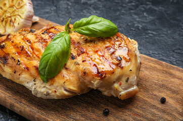 Board with cooked chicken fillet on dark background