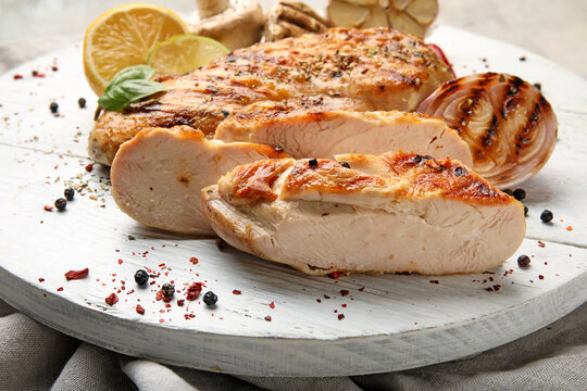 Board with cooked chicken fillet and vegetables on table