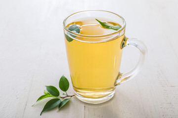 Cup of hot aromatic tea and green tea leaves on table