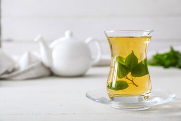 Cup of hot aromatic tea with green tea leaves on table