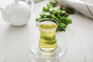 Cup of hot aromatic tea with green tea leaves on table