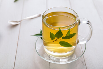 Cup of hot aromatic tea and green tea leaves on table