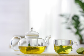 Teapot and cup of tasty mint tea on blurred background