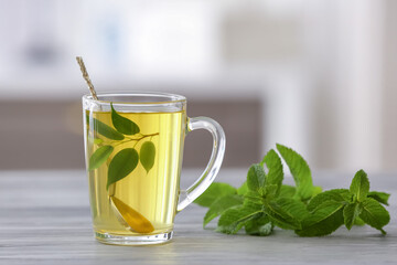 Cup of tea with spoon, green tea leaves and mint on blurred background