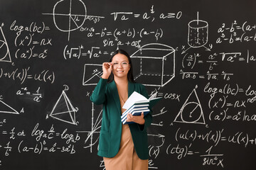 Asian female teacher near blackboard in classroom