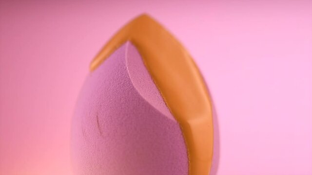 Makeup liquid foundation pouring on make-up blender sponge, closeup. Foundation beauty facial cosmetics, tool for perfect make up. Dripping bb cream or concealer. Over pink background.