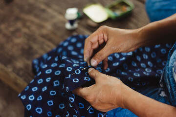 Woman's hands sewing running stitch in blue tribal fabric (dyed indigo color). folk art, crafts.