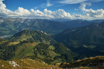 Aerial panoramic view of beautiful countryside with green hills and mountain ranges in the background and cloudy blue sky above on a sunny day in Chur, Switzerland.