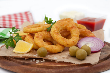 Deep fried squid or fish rings appetizer. Breaded squid or fish rings with lemon,  ketchup and mayonezze. Golden, crunchy calamari snack on white background.