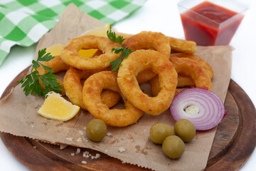 Deep fried squid or fish rings appetizer. Breaded squid or fish rings with lemon,  olives and ketchup. Golden, crunchy calamari snack.