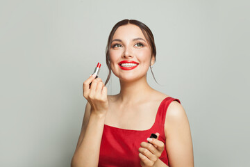 Pretty young woman holding red lipstick near lips and smiling on white background