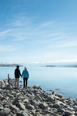 Fototapeta na wymiar Couple standing on the shore of Lake Tekapo with snow-capped mountains in the distance, portrait format