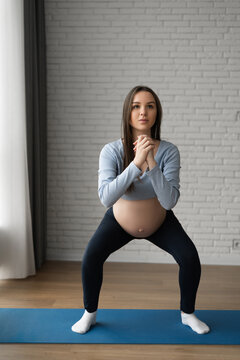 Beautiful pregnant woman doing exercises at home. looks at the camera and crouches.
