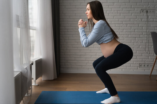 Beautiful pregnant woman doing exercises at home. Squats.