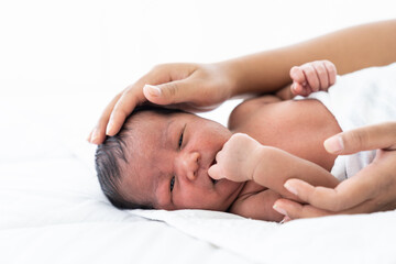 Fototapeta na wymiar African American newborn baby or infant lying on white bed while mother’s hands takes care and comforting. Family, love and new life concept