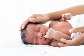 African American newborn baby or infant lying on white bed while mother’s hands takes care and comforting. Family, love and new life concept