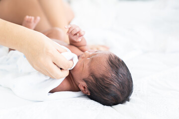 Mom wiping her newborn baby skin, face with wet wipes carefully on bed at home. family, cleaning wipe and infant concept