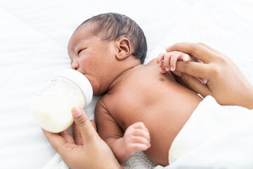 African American newborn baby eating milk from nipples from mother arms. Mother feeding her infant with milk bottle